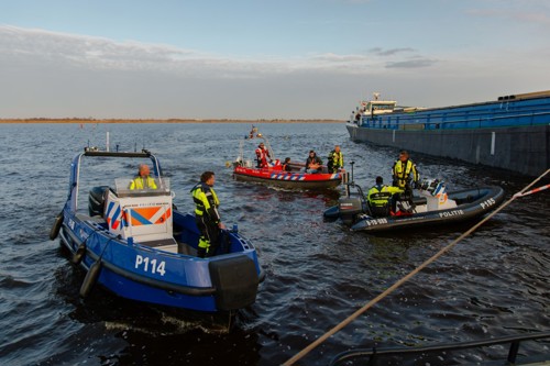 Verschillende boten van hulpdiensten liggen in het water en de hulpverleners overleggen met elkaar.