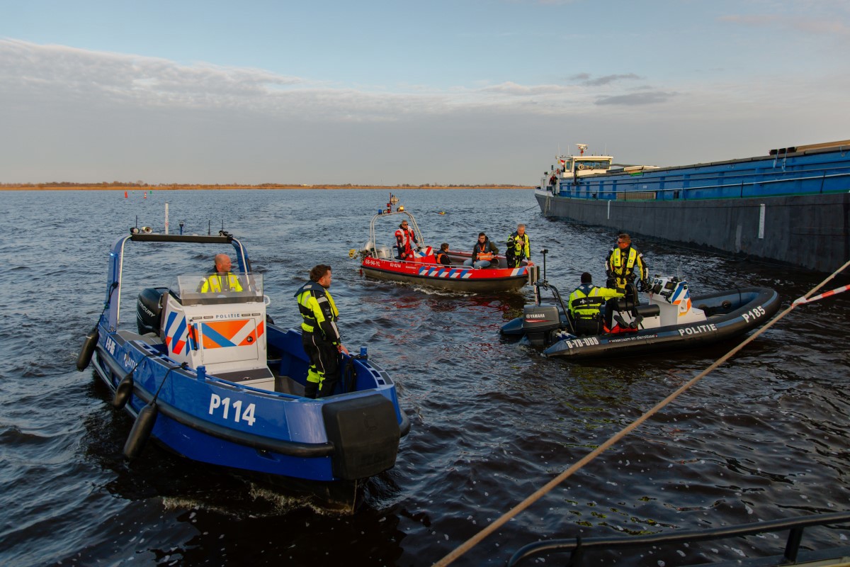 Verschillende boten van hulpdiensten liggen in het water en de hulpverleners overleggen met elkaar.