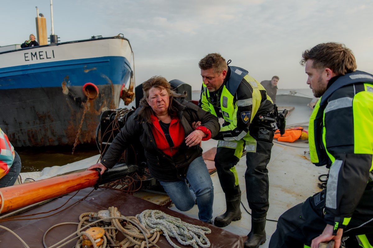 Twee hulpverleners helpen een vrouw van het skûtsje af.